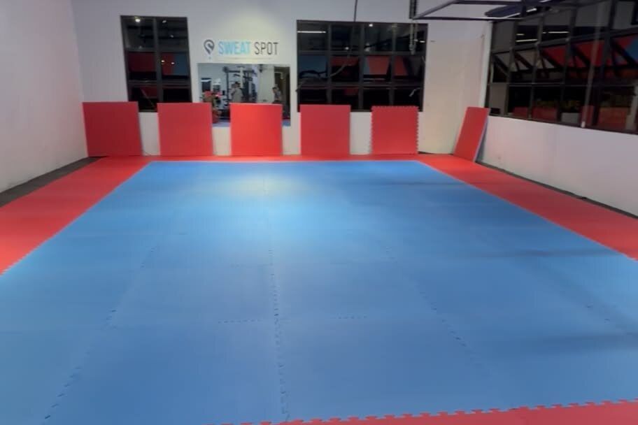 Empty jiu-jitsu room with blue and red puzzle mats, red wall pads, and the Sweat Spot sign on the back wall