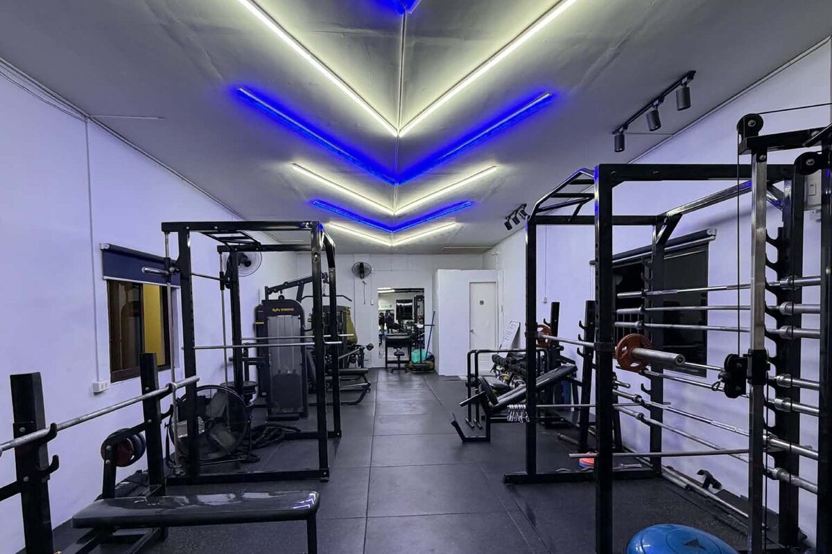 Weight room with squat racks and benches under a blue and white LED ceiling